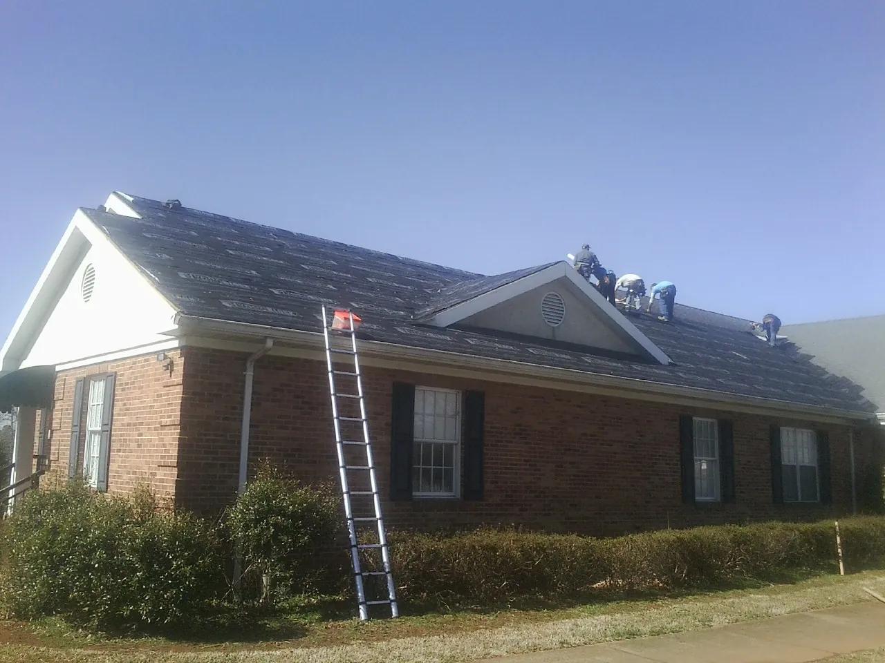 Crew tearing shingles off a brick ranch roof with a ladder set — Emergency Roof Repair work by our crew in Kent